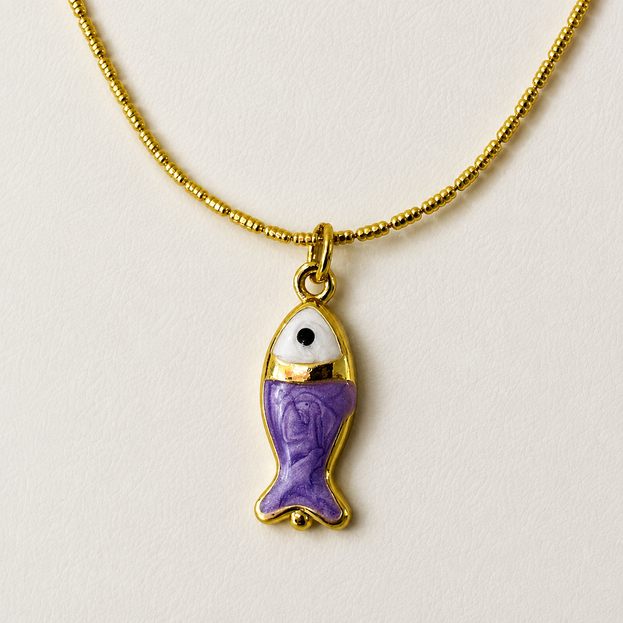 Collar dorado en chapa de oro 18k con dije de pez y detalle decorativo morado. Mayoreo 